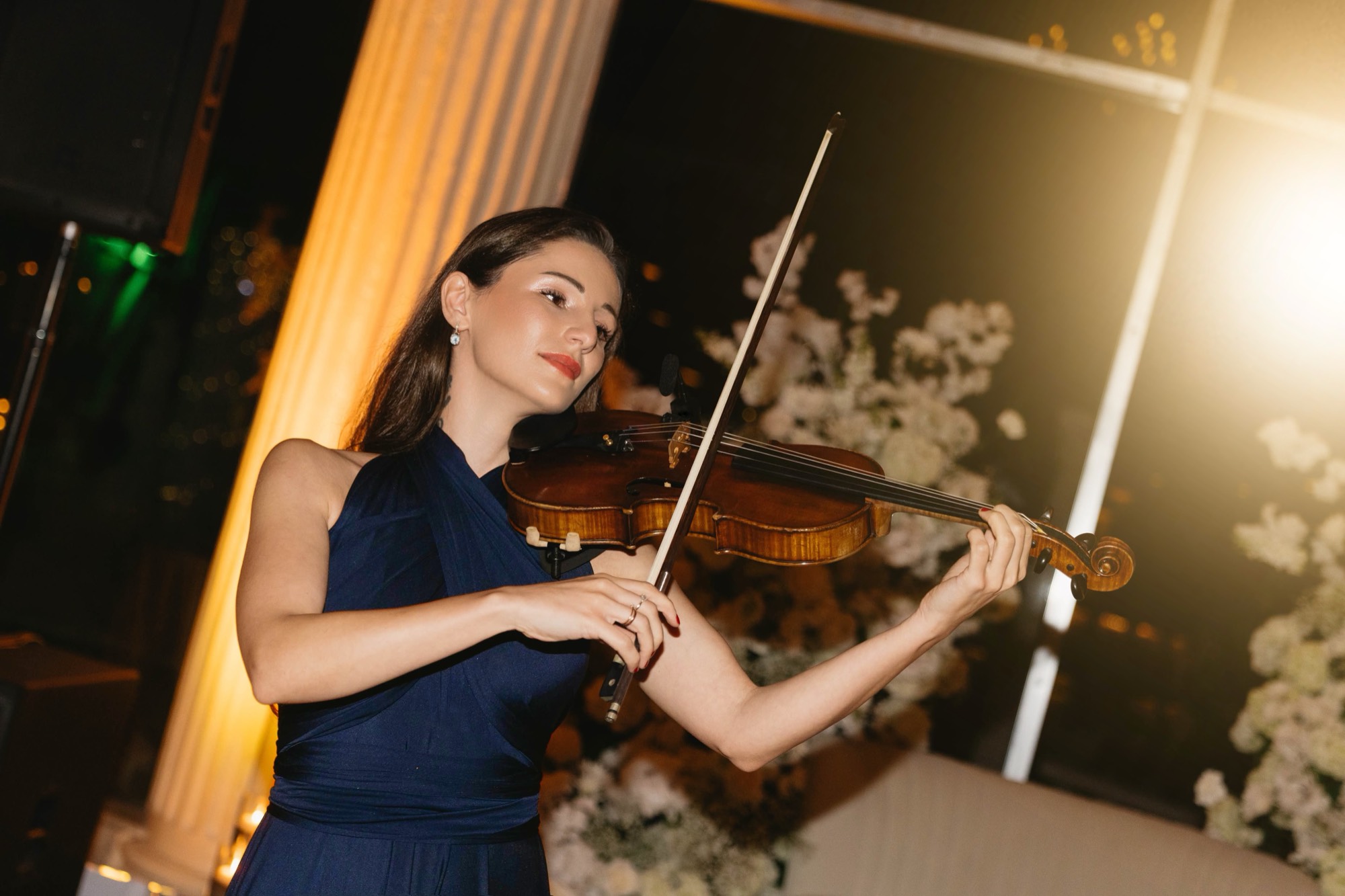 Tatev Muradyan in a navy dress playing violin at an evening wedding reception with white flowers