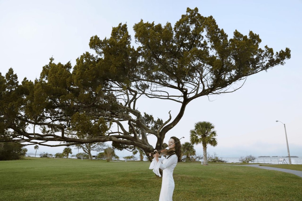 Tatev Muradyan with her violin beneath a large tree by the water
